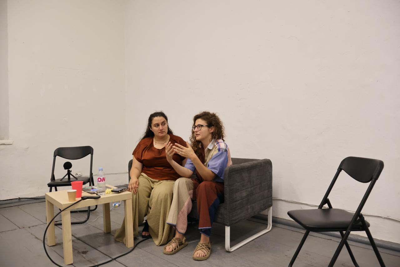 two people sitting on a sofa in an art space